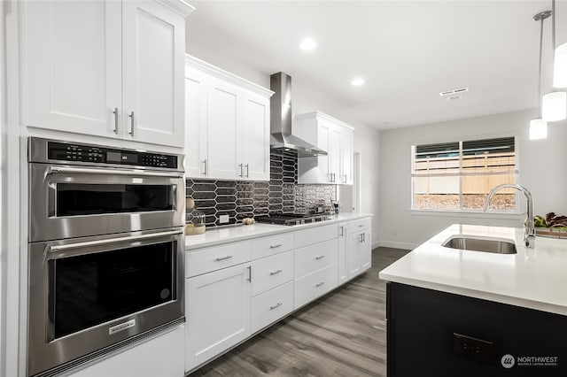 kitchen with sink, stainless steel appliances, wall chimney range hood, pendant lighting, and white cabinets