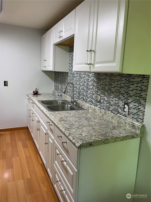 kitchen featuring light stone counters, light hardwood / wood-style floors, tasteful backsplash, white cabinets, and sink