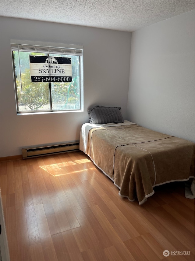 bedroom with a baseboard heating unit, light hardwood / wood-style flooring, and a textured ceiling