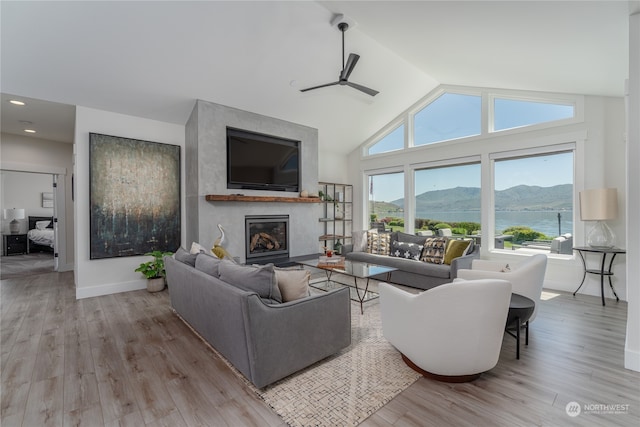 living room with light hardwood / wood-style flooring, a fireplace, ceiling fan, high vaulted ceiling, and a water and mountain view