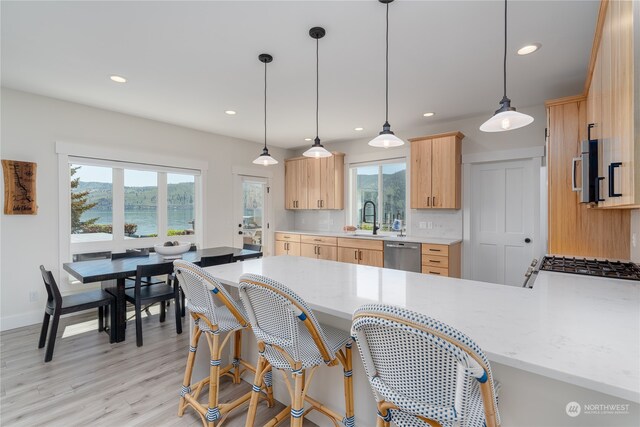 kitchen with light brown cabinets, light hardwood / wood-style flooring, dishwasher, hanging light fixtures, and tasteful backsplash