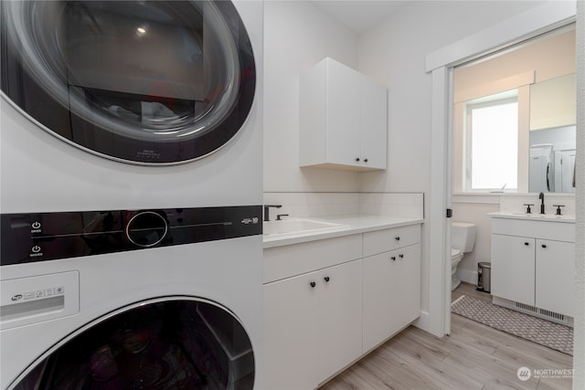 laundry room with stacked washing maching and dryer, light hardwood / wood-style floors, and sink