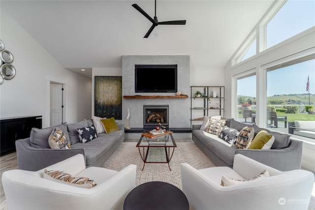 living room featuring a premium fireplace, ceiling fan, light wood-type flooring, and high vaulted ceiling