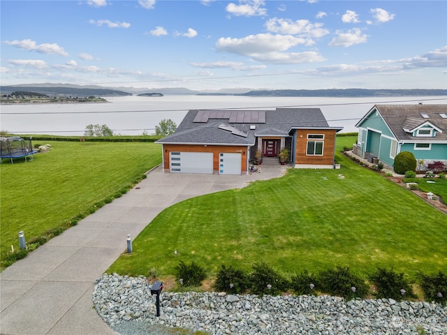 view of front of home featuring solar panels, a trampoline, a front yard, a garage, and a water view