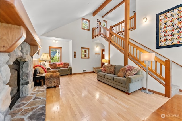 living room with hardwood / wood-style floors, a stone fireplace, a wealth of natural light, and high vaulted ceiling