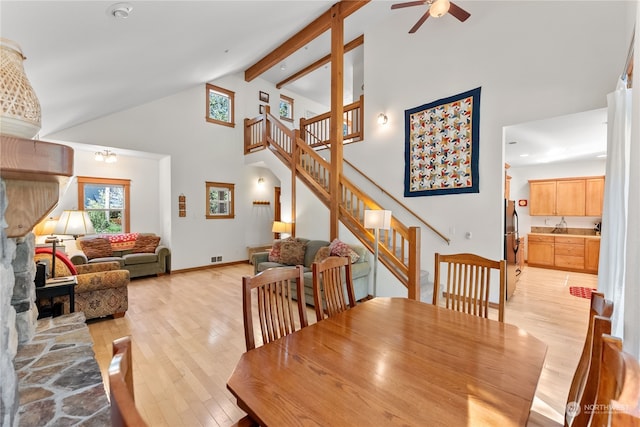 dining room with high vaulted ceiling, ceiling fan with notable chandelier, light hardwood / wood-style floors, and beamed ceiling