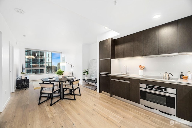 kitchen featuring stainless steel oven, cooktop, light wood-type flooring, and sink