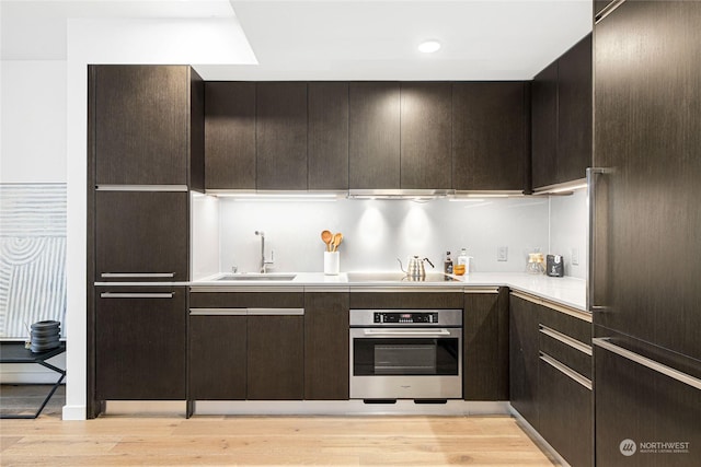 kitchen featuring dark brown cabinetry, sink, baseboard heating, oven, and light wood-type flooring