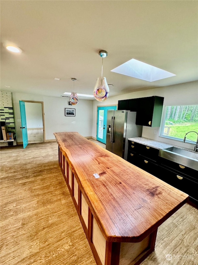 kitchen featuring sink, decorative light fixtures, a skylight, light hardwood / wood-style flooring, and stainless steel fridge