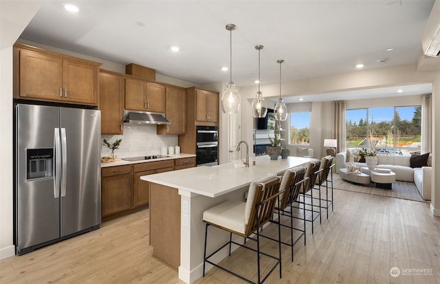 kitchen with pendant lighting, a kitchen breakfast bar, a kitchen island with sink, light hardwood / wood-style floors, and black appliances