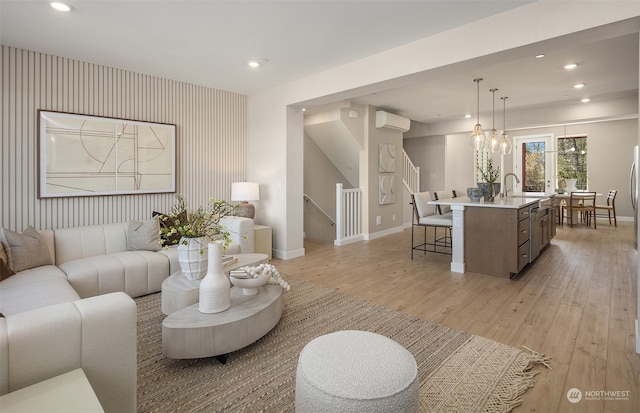 living room featuring an AC wall unit, sink, a notable chandelier, and light hardwood / wood-style flooring