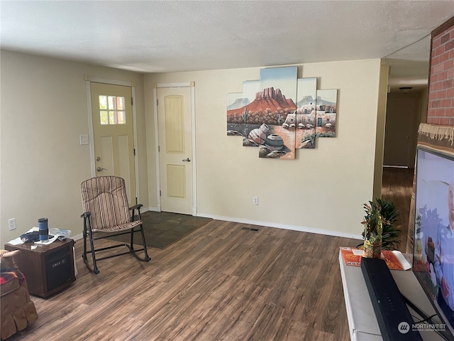 living area with wood-type flooring, brick wall, and a textured ceiling