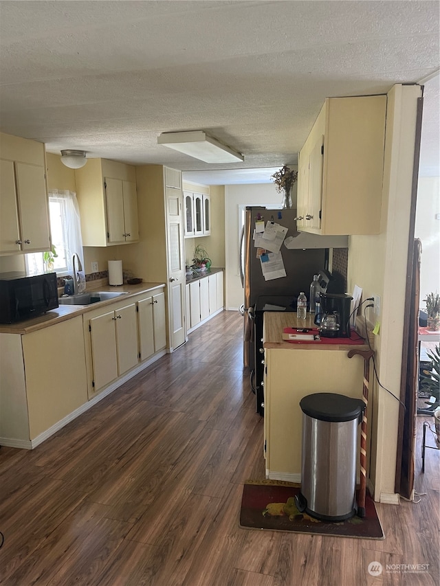 kitchen featuring stainless steel refrigerator, sink, hardwood / wood-style flooring, cream cabinetry, and a textured ceiling