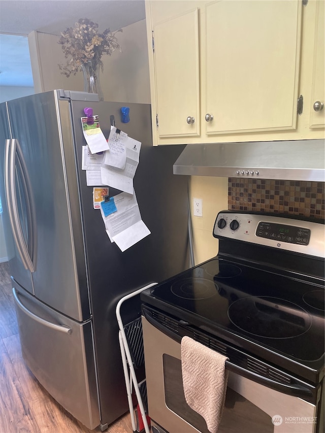 interior space with light hardwood / wood-style floors, appliances with stainless steel finishes, wall chimney range hood, and backsplash