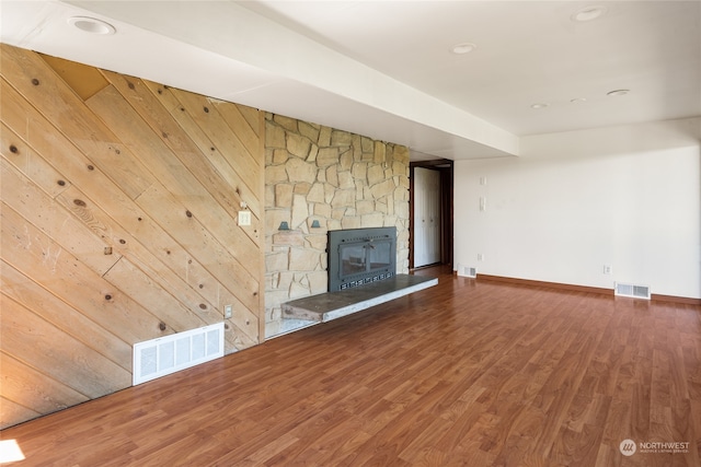 unfurnished living room with dark hardwood / wood-style floors, wooden walls, and a stone fireplace