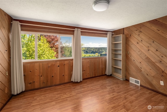 unfurnished room with wooden walls, light hardwood / wood-style flooring, and a textured ceiling