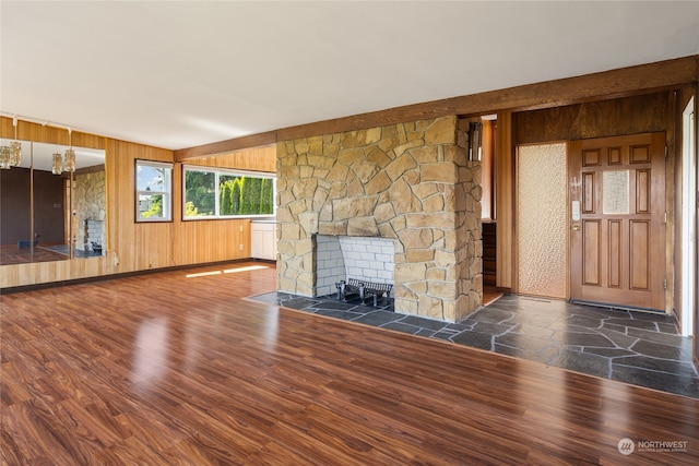 unfurnished living room featuring dark wood-type flooring, a stone fireplace, and wooden walls