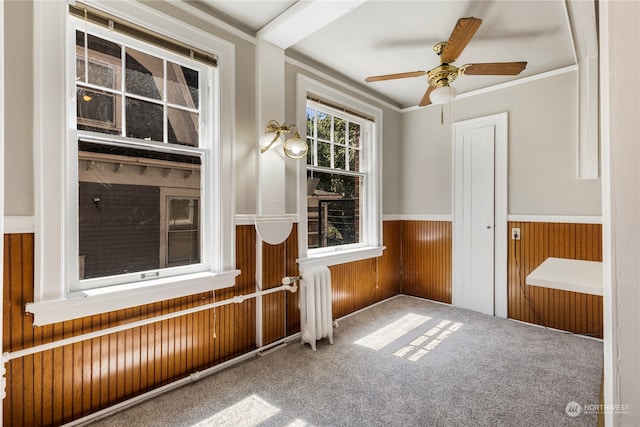 unfurnished sunroom featuring ceiling fan, radiator heating unit, and beam ceiling