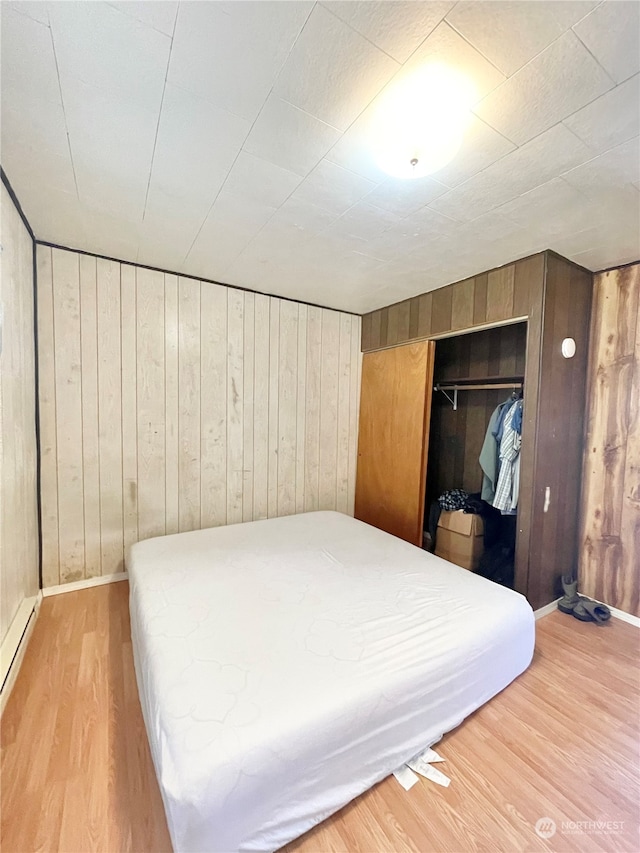 bedroom with a closet, wooden walls, and light wood-type flooring