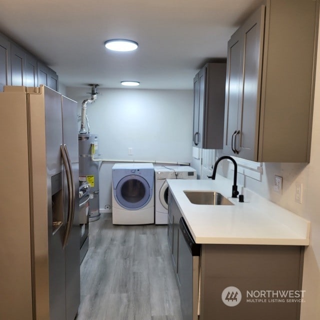 laundry area featuring secured water heater, cabinets, light hardwood / wood-style floors, washer and dryer, and sink