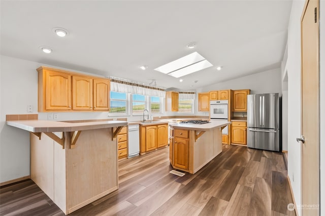 kitchen with appliances with stainless steel finishes, vaulted ceiling with skylight, hardwood / wood-style flooring, and a kitchen breakfast bar