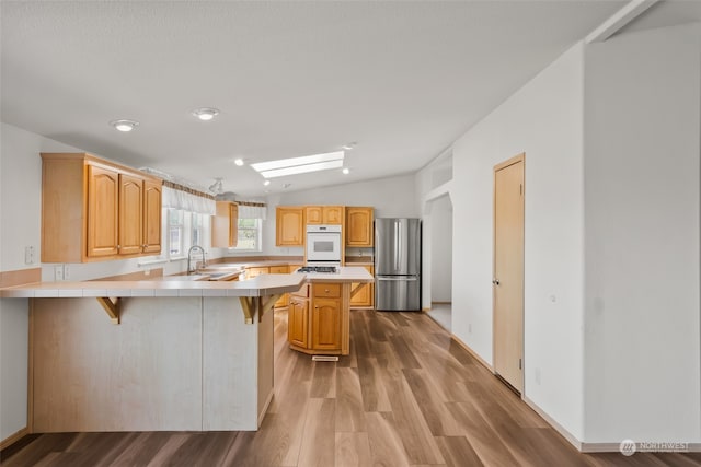 kitchen with kitchen peninsula, stainless steel appliances, lofted ceiling with skylight, a kitchen breakfast bar, and hardwood / wood-style floors