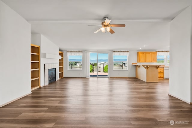 unfurnished living room with ceiling fan, a tile fireplace, dark hardwood / wood-style floors, and built in shelves