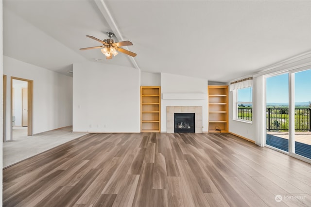 unfurnished living room with built in features, ceiling fan, lofted ceiling, a tile fireplace, and hardwood / wood-style floors