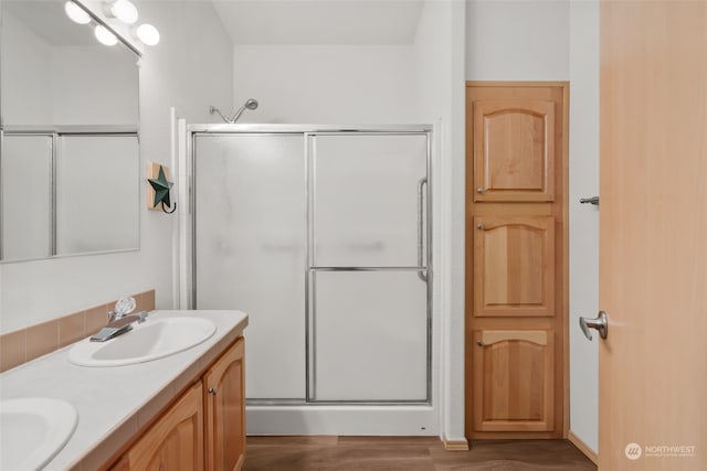 bathroom with wood-type flooring, a shower with shower door, and dual vanity