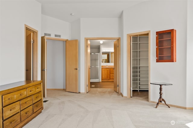 bedroom featuring light colored carpet, a closet, a walk in closet, and ensuite bath