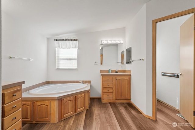 bathroom featuring a tub, hardwood / wood-style floors, vaulted ceiling, and vanity with extensive cabinet space