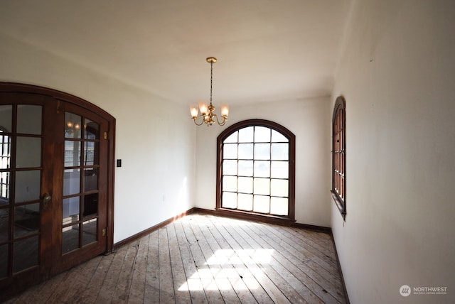 empty room with french doors, an inviting chandelier, and hardwood / wood-style flooring