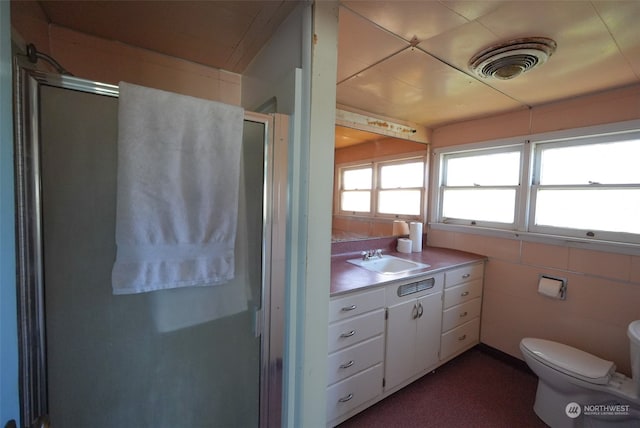 bathroom with tile walls, a shower with door, vanity, and toilet