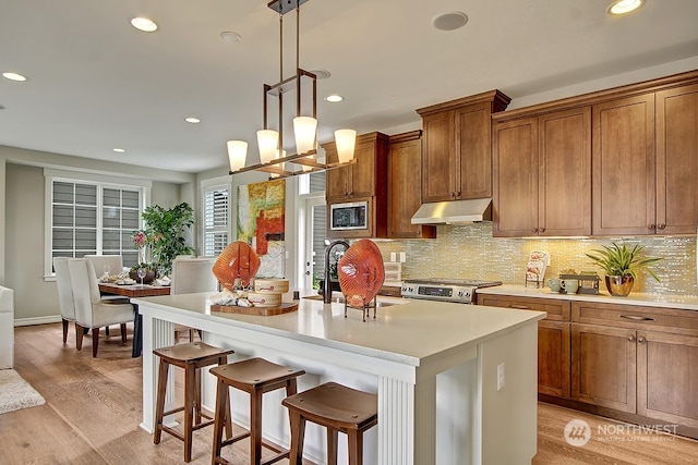 kitchen featuring stainless steel range, a notable chandelier, light hardwood / wood-style floors, hanging light fixtures, and an island with sink