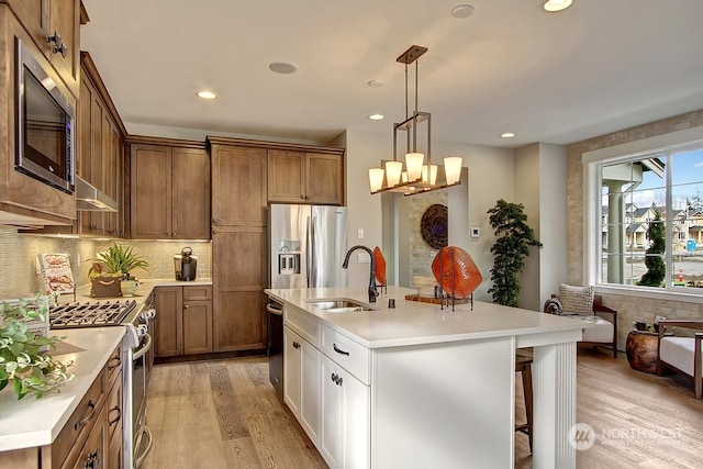 kitchen featuring a center island with sink, sink, light wood-type flooring, appliances with stainless steel finishes, and white cabinetry