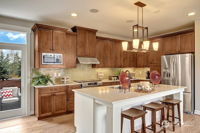 kitchen with stainless steel appliances, sink, pendant lighting, a center island with sink, and light hardwood / wood-style flooring