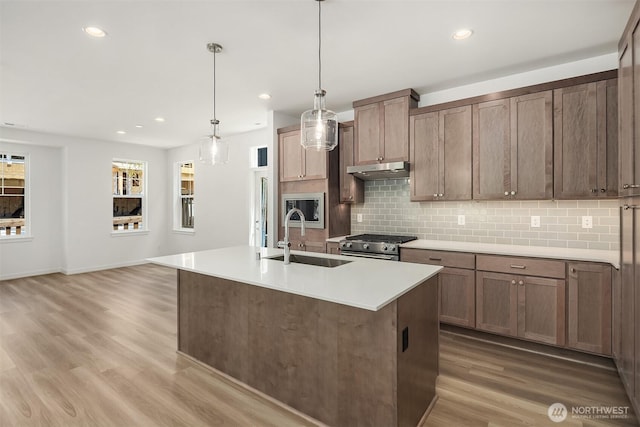 kitchen with high end stainless steel range, light countertops, a sink, an island with sink, and under cabinet range hood