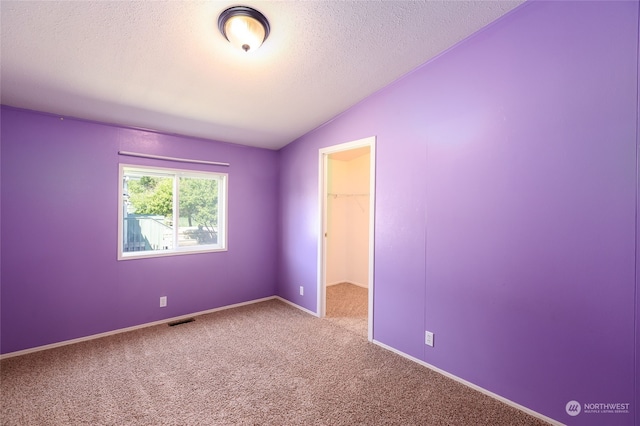 carpeted empty room featuring visible vents, baseboards, a textured ceiling, and vaulted ceiling