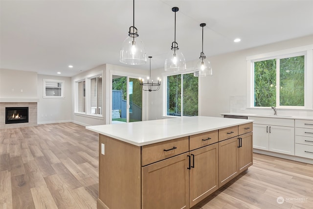 kitchen featuring hanging light fixtures, light brown cabinetry, light wood-type flooring, a fireplace, and a center island