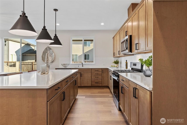 kitchen featuring appliances with stainless steel finishes, sink, light wood-type flooring, pendant lighting, and decorative backsplash