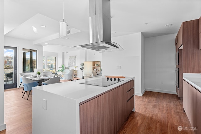 kitchen with island range hood, black electric stovetop, hanging light fixtures, and hardwood / wood-style flooring