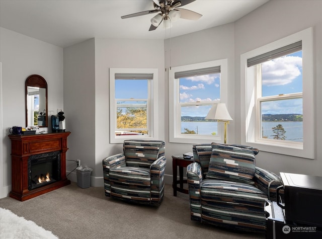 sitting room with a high end fireplace, ceiling fan, carpet flooring, and a water view