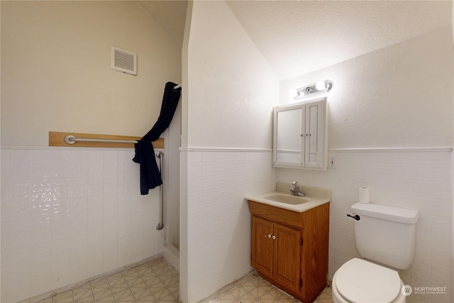 bathroom featuring lofted ceiling, toilet, vanity, and tile walls