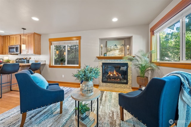 living area featuring baseboards, a glass covered fireplace, light wood-style flooring, and recessed lighting