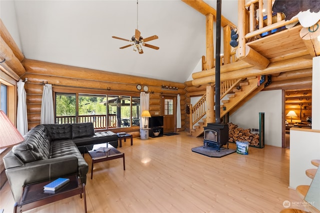 living room with ceiling fan, wood-type flooring, a wood stove, rustic walls, and high vaulted ceiling