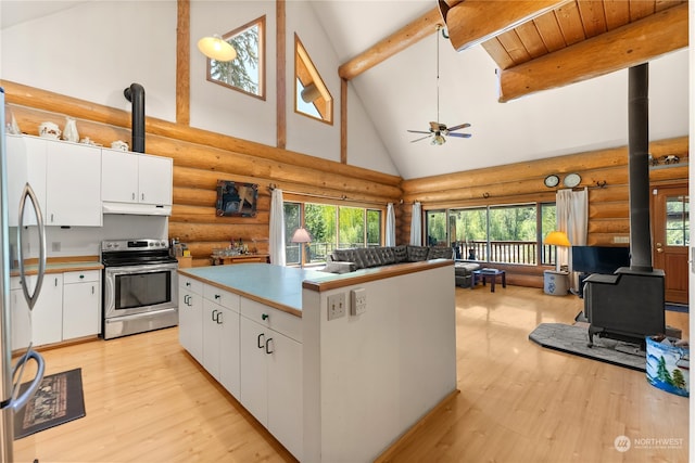 kitchen with a wood stove, high vaulted ceiling, white cabinets, rustic walls, and appliances with stainless steel finishes