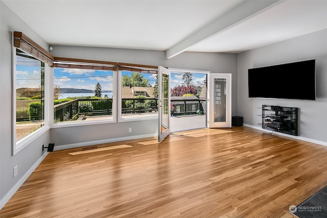 unfurnished living room featuring beam ceiling and light hardwood / wood-style floors