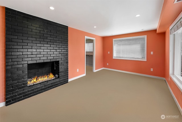 unfurnished living room with plenty of natural light, carpet, and a brick fireplace