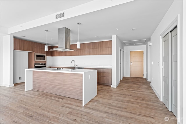 kitchen featuring island exhaust hood, black appliances, pendant lighting, light hardwood / wood-style floors, and an island with sink