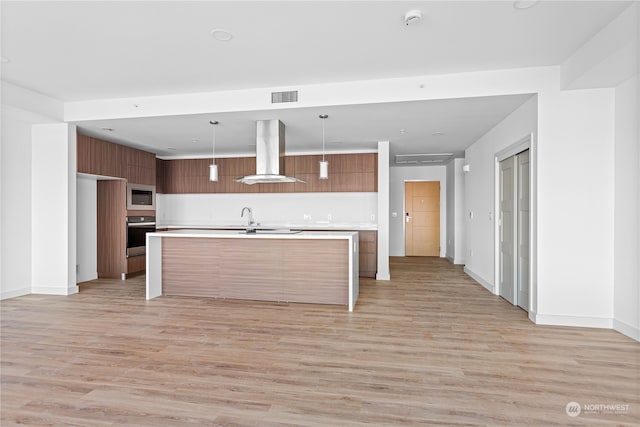 kitchen with pendant lighting, a center island with sink, white microwave, island exhaust hood, and oven